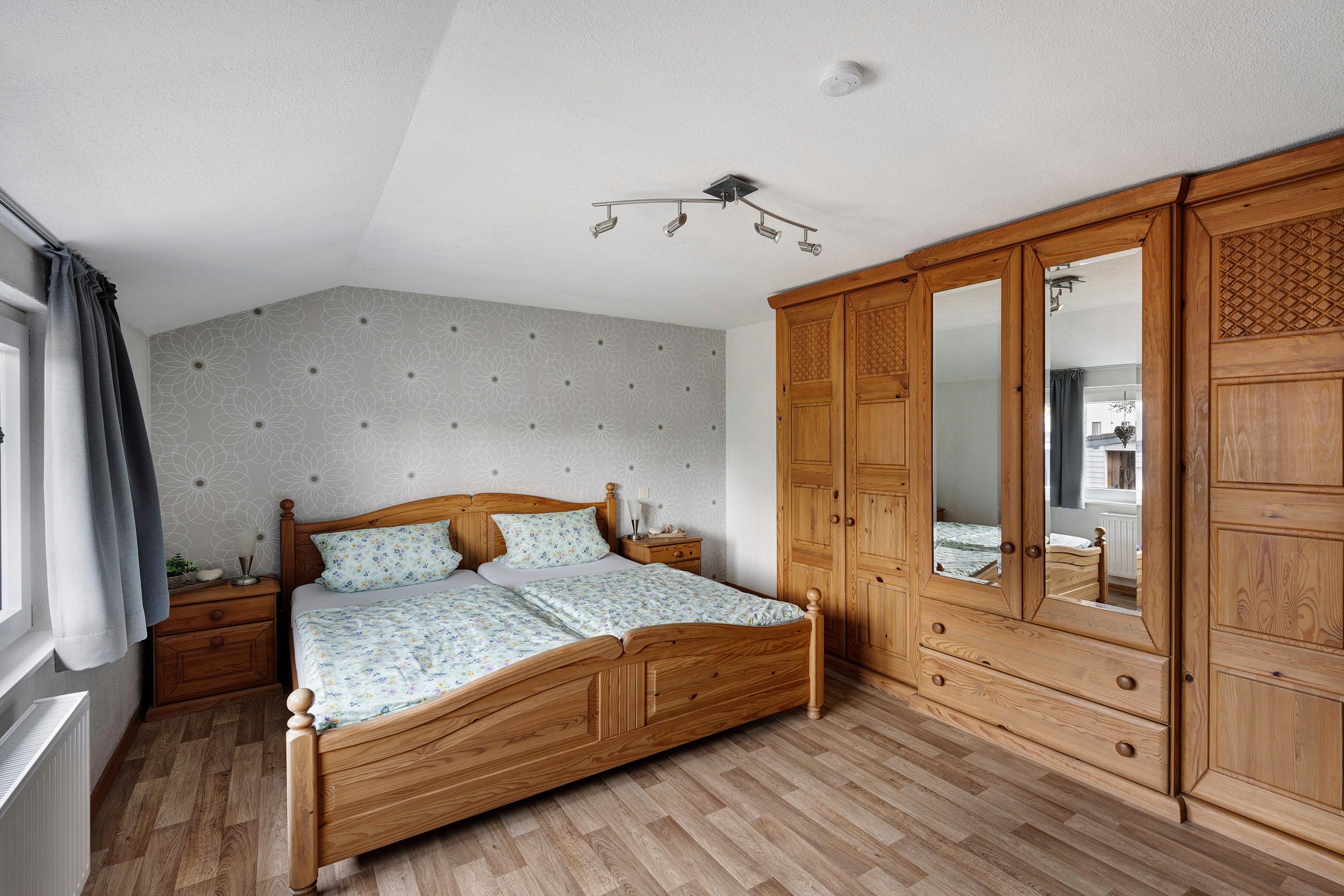Ein Schlafzimmer mit einem hölzernen Bett, einem Nachttisch, einem Kleiderschrank und einer Deckenleuchte.