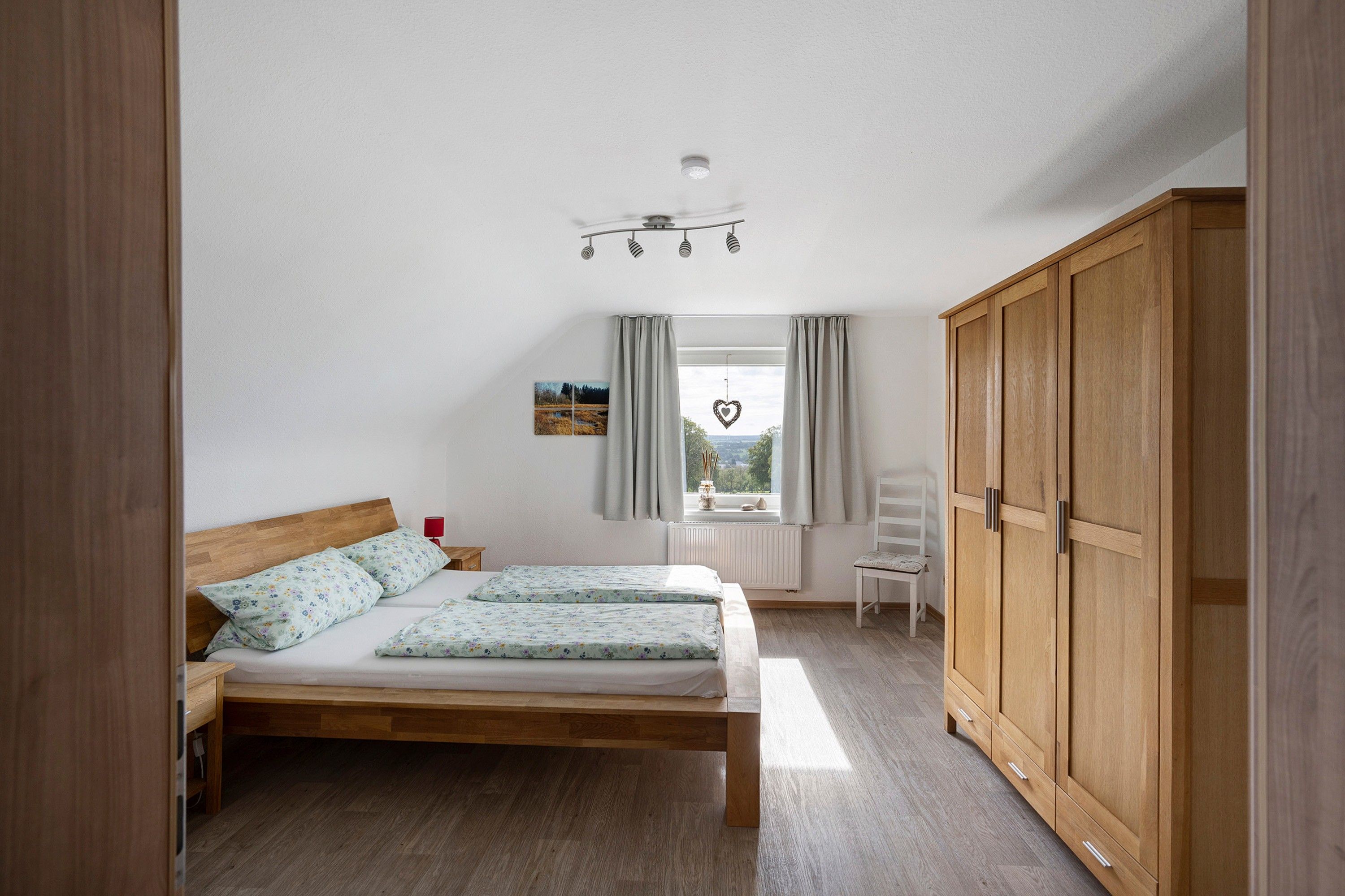Une chambre à coucher avec un lit en bois, une armoire, une fenêtre avec des rideaux et un luminaire au plafond.
