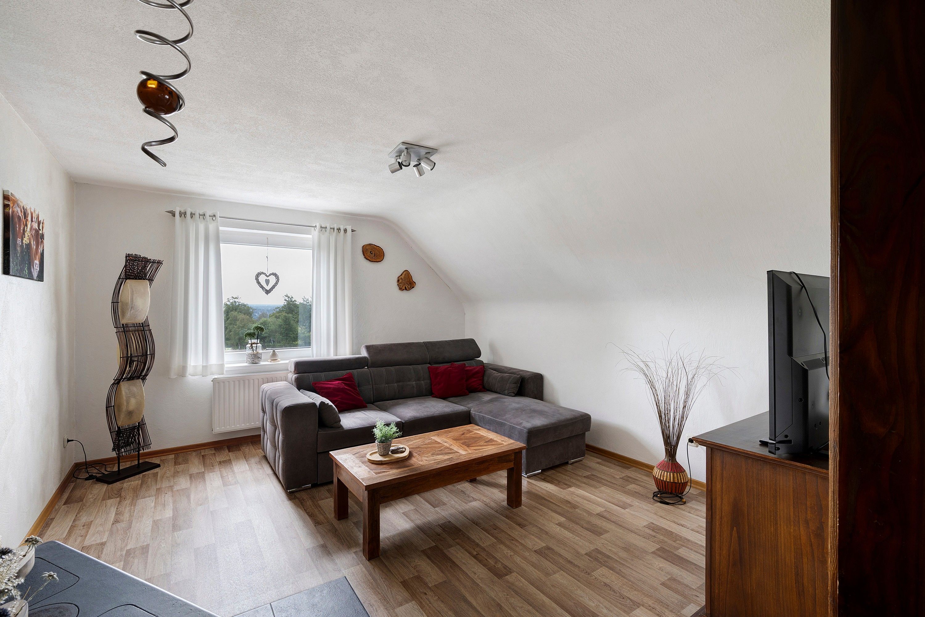 Een moderne woonkamer met een grijze hoekbank, een houten salontafel en een televisie op een houten dressoir.