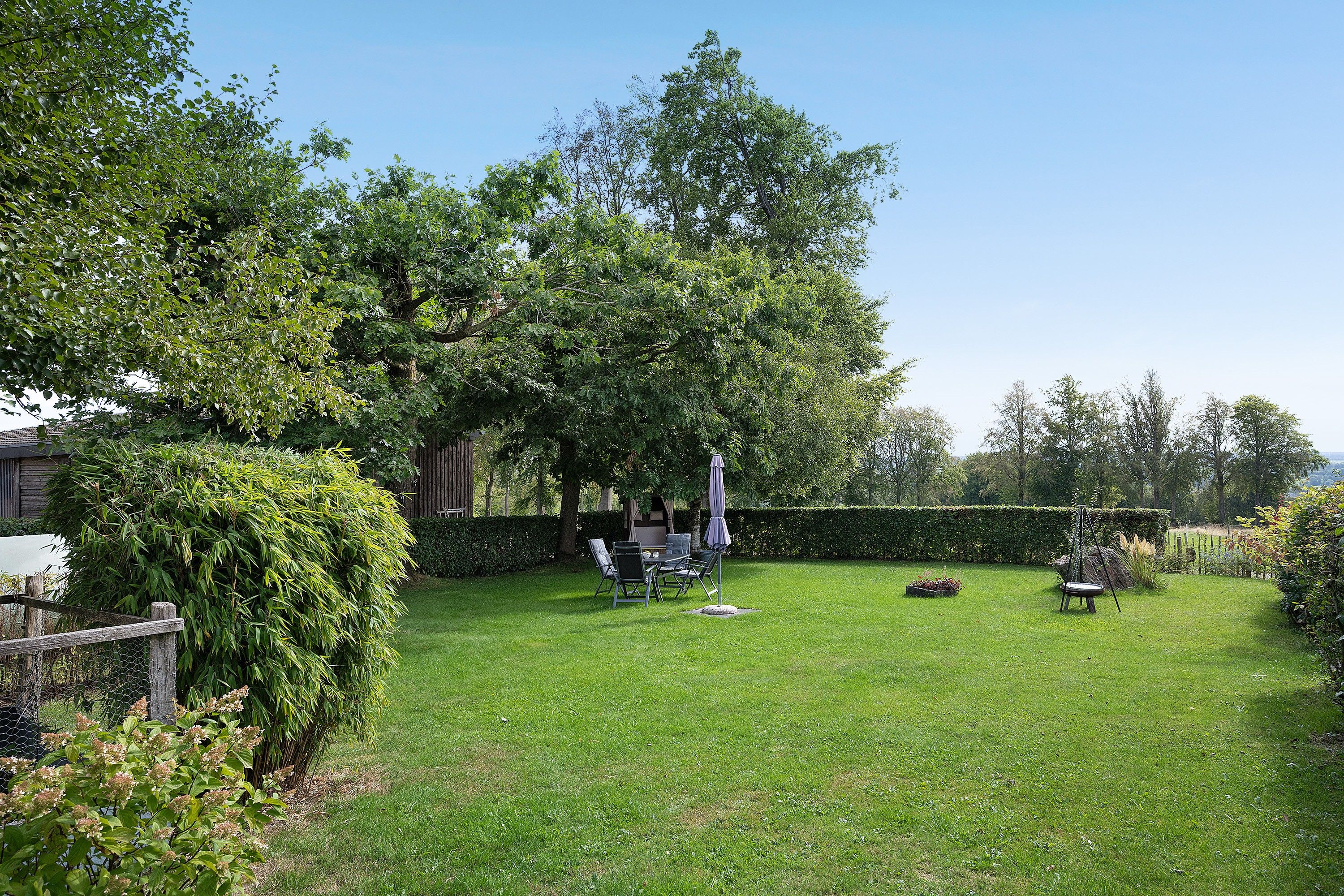 Un jardin bien entretenu, agrémenté d’un espace repas, d’une balançoire et d’une variété d’arbres et d’arbustes.
