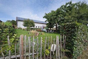A white building with a sloped roof, surrounded by a wooden fence and lush greenery. - Apartment 'Ferienwohnung Hohes Venn' with Wi-Fi (Monschau)
