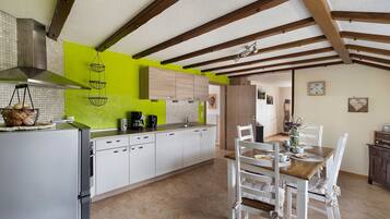 Une cuisine avec des meubles blancs, un mur d’accent vert, un luminaire suspendu et un coin repas avec des chaises blanches et une table en bois.