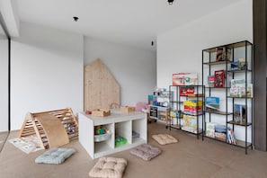 Un espace de jeux pour enfants avec une table blanche, des étagères de rangement et une structure d’escalade en bois.