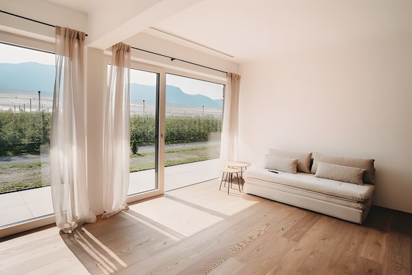 Ein modernes Zimmer mit einer großen Schiebeglaswand, Holzboden, einem weißen Sofa und einem kleinen runden Tisch.