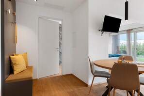 Une pièce moderne avec un plancher en bois, une table ronde et un téléviseur fixé au mur.