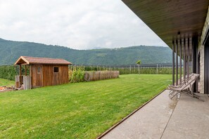 A wooden cabin with a sloped roof, a grassy yard, a paved patio, and a view of a mountain range. - Apartment 'Grafferhof II' with Mountain View, Wi-Fi and Air Conditioning (Bolzano)