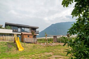 Ein modernes Haus mit großem Fenster, einem hölzernen Spielhäuschen und einer gelben Rutsche im Garten.