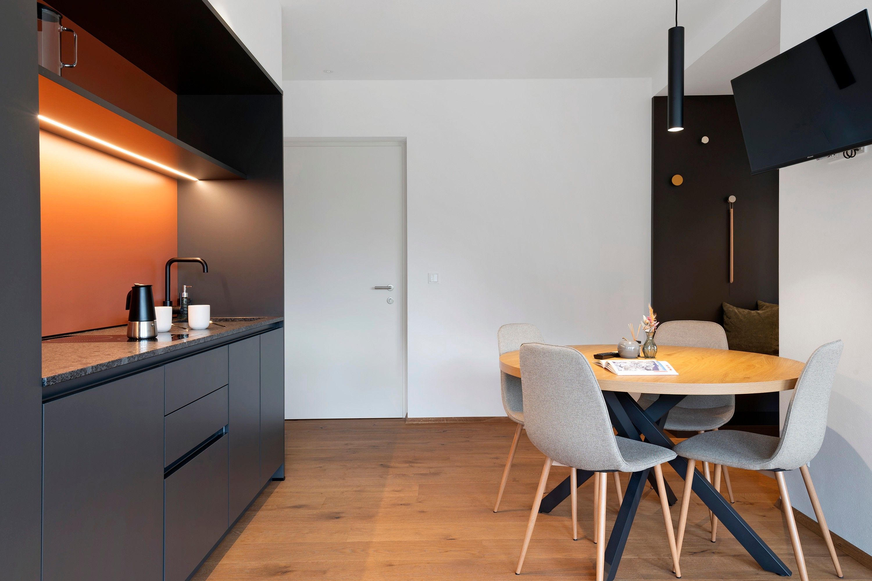 Een moderne keuken met een inbouwoven, een koffieapparaat en een eethoek met een ronde tafel en stoelen.