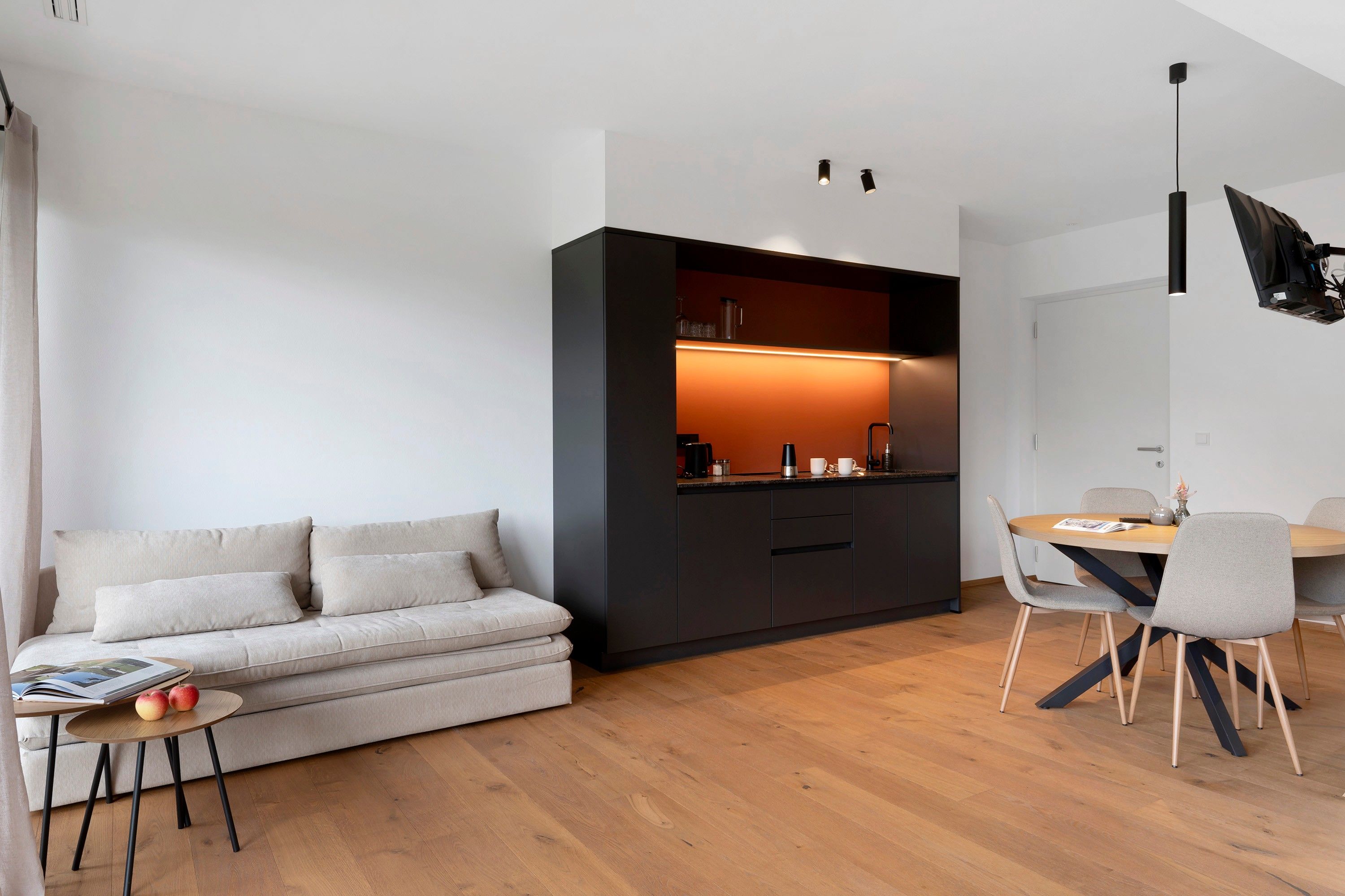 Een moderne woonruimte met een bank, een eettafel met stoelen en een keuken met een aanrecht en kastjes.