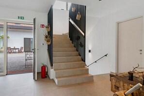 Eine Treppe mit Handlauf, einem Feuerlöscher und einer Tür zu einem Außenbereich mit Stühlen und einem Tisch.