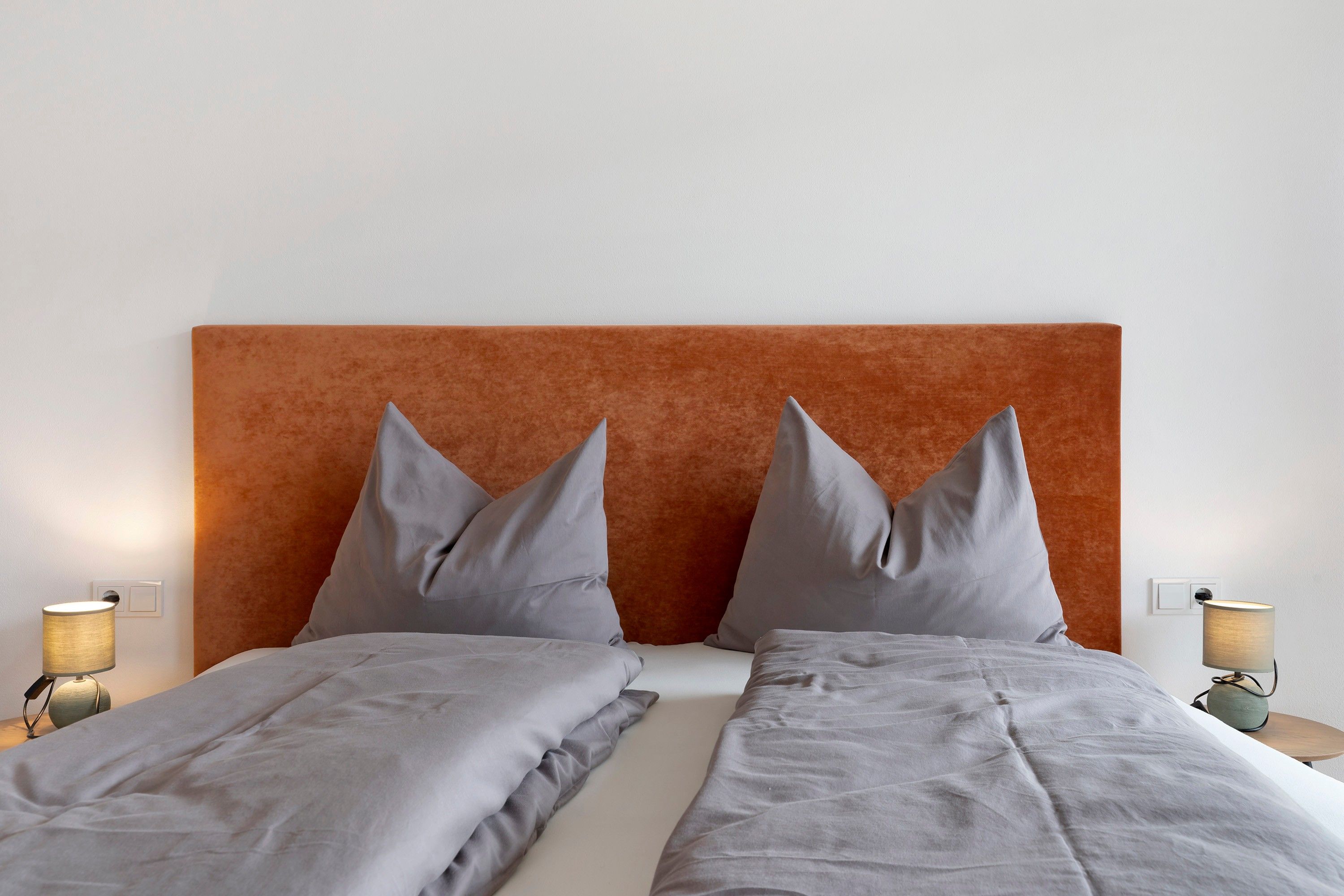 Ein Doppelbett mit Kopfteil, zwei Nachttische mit Lampen und eine Wand in neutraler Farbe.