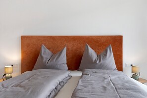Un lit double avec une tête de lit, deux lampes de chevet et un mur aux couleurs neutres.