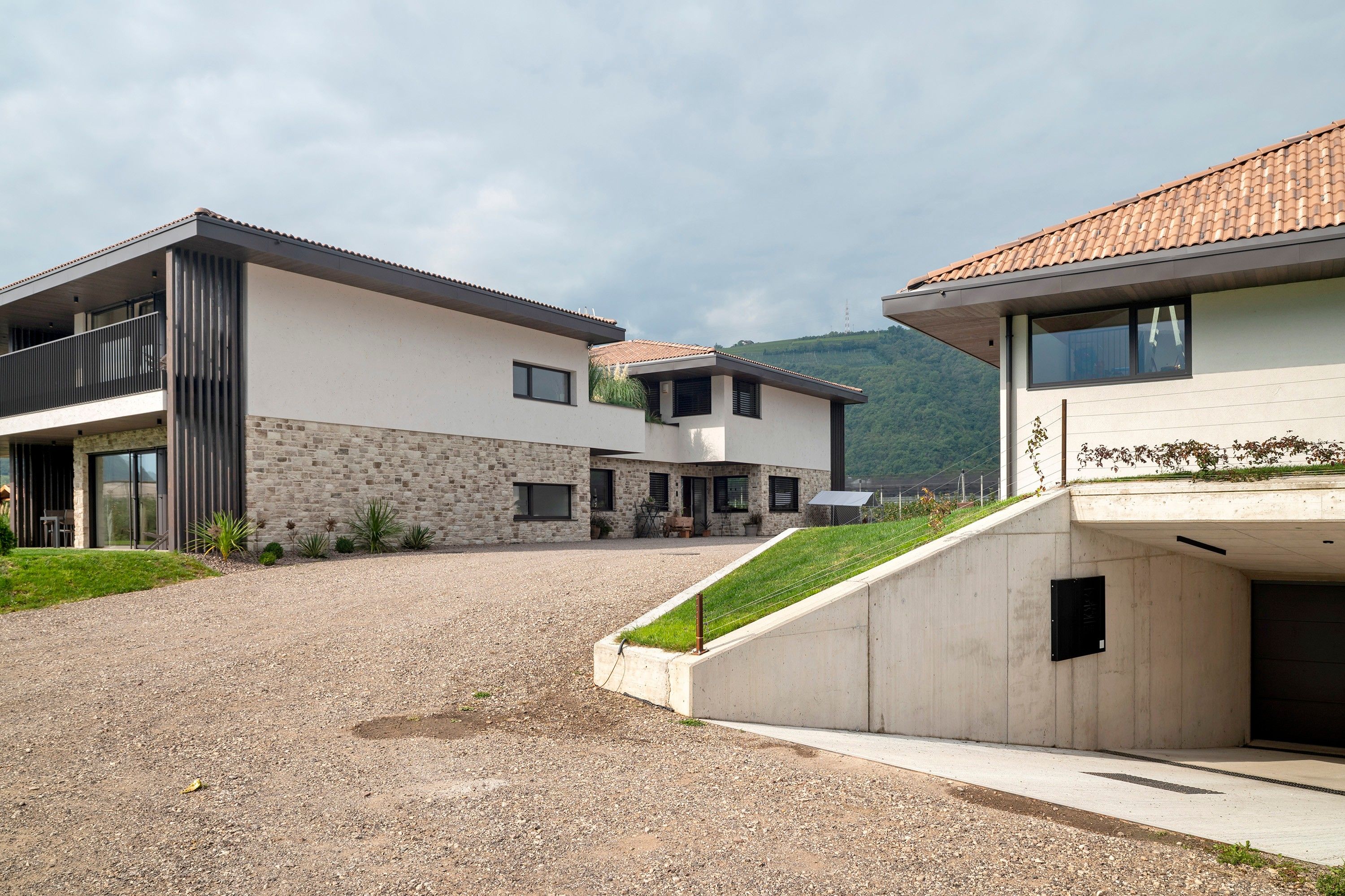 Um edifício residencial moderno com entrada de cascalho, fachada de pedra e vista para uma paisagem montanhosa.
