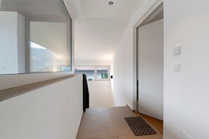 Un couloir étroit, avec une fenêtre sur le côté gauche, une porte sur le côté droit et un petit tapis au bout.