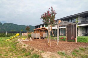 A playground with a slide and swings, a wooden playhouse, and a building with a balcony. - Apartment 'Grafferhof IV' with Mountain View, Wi-Fi, and Air Conditioning (Bolzano)