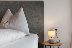 A neatly made bed with pillows, a bedside lamp, and a small round table with a lamp on it. - Apartment 'Grafferhof IV' with Mountain View, Wi-Fi, and Air Conditioning (Bolzano)