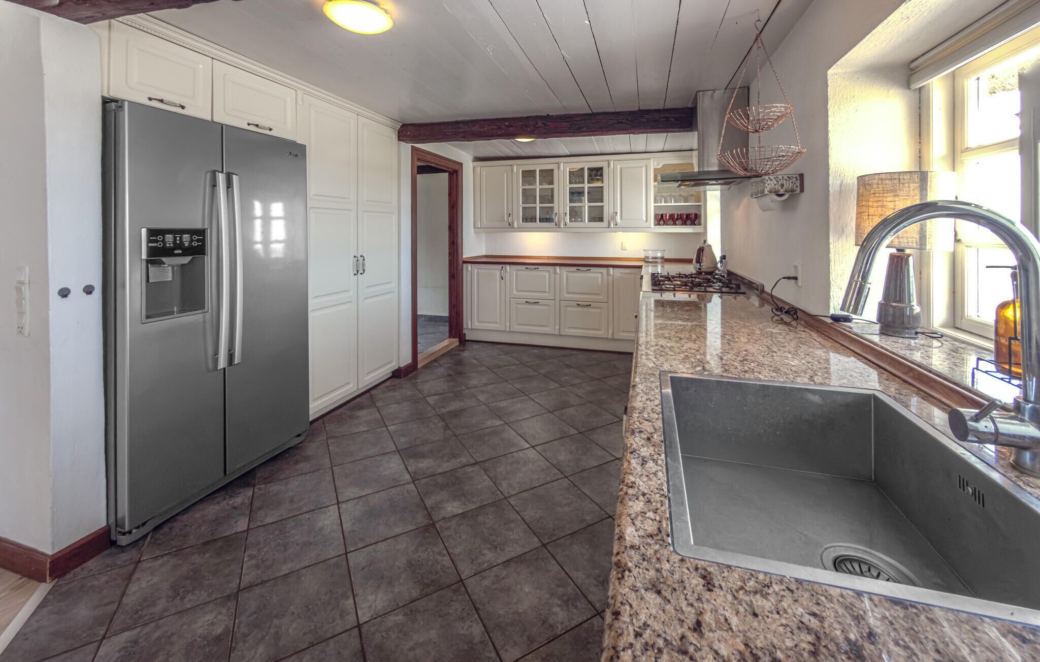 A kitchen with a stainless steel refrigerator, granite countertops, a sink, and white cabinetry.