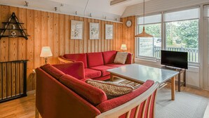 Ett mysigt rum med en röd soffa, ett träbord och en tv som står på ett stativ.