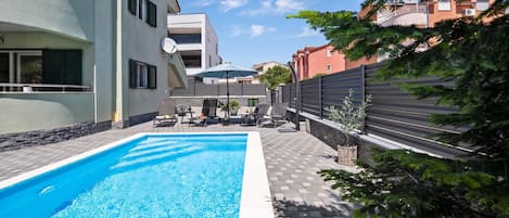 A swimming pool with lounge chairs and umbrellas, surrounded by a paved patio area.