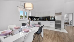 A modern kitchen with white cabinets, a stainless steel refrigerator, and a dining area with pink plates and white chairs. - S Villa With Pool, Jacuzzi & Gym (Vodice)
