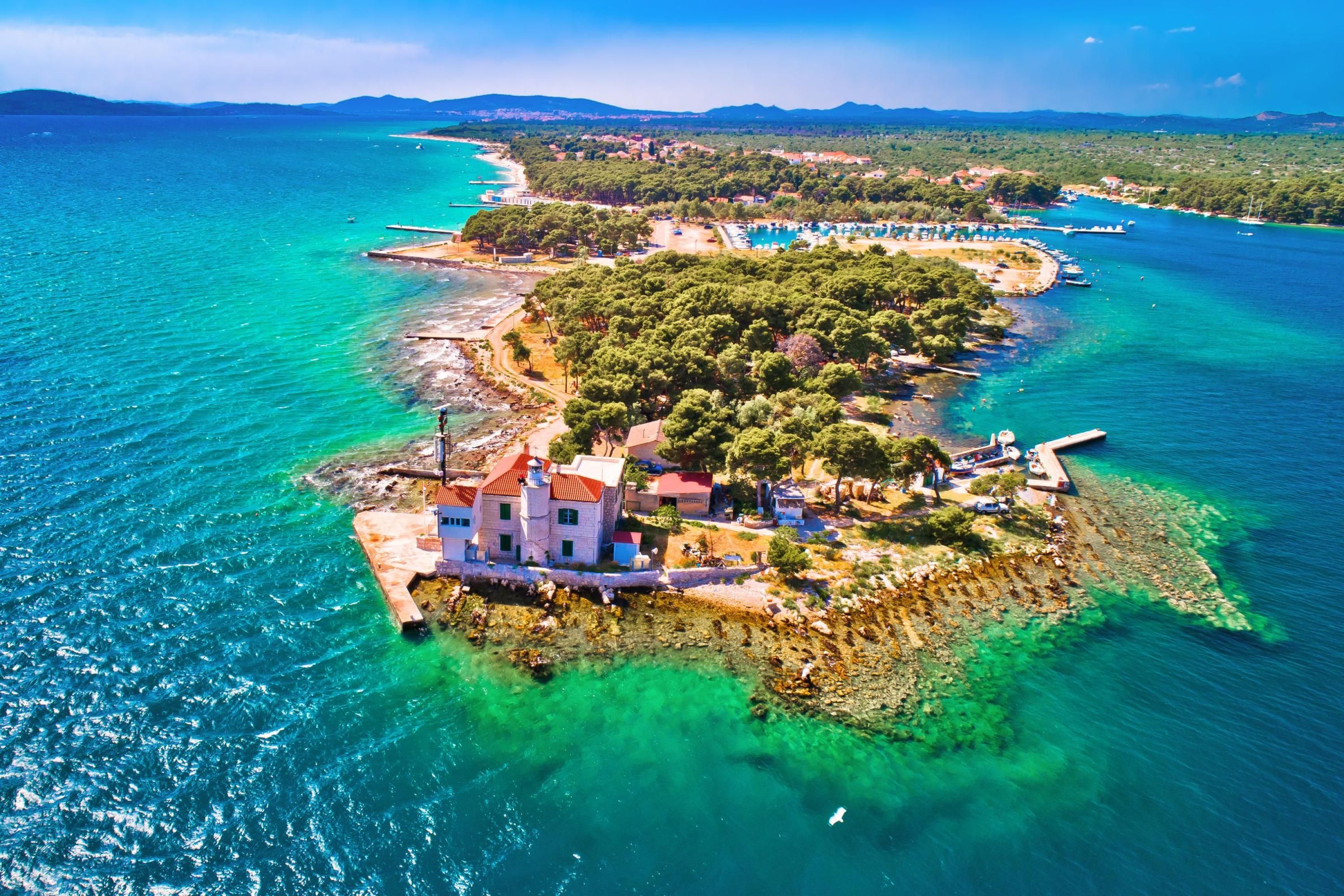 Une vue aérienne d’une propriété située sur la côte, avec un bâtiment imposant, des eaux turquoise d’une clarté exceptionnelle et un paysage verdoyant luxuriant.