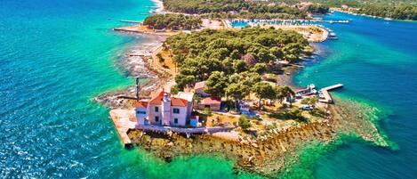 An aerial view of a coastal property with a prominent building, clear turquoise waters, and a lush green landscape.