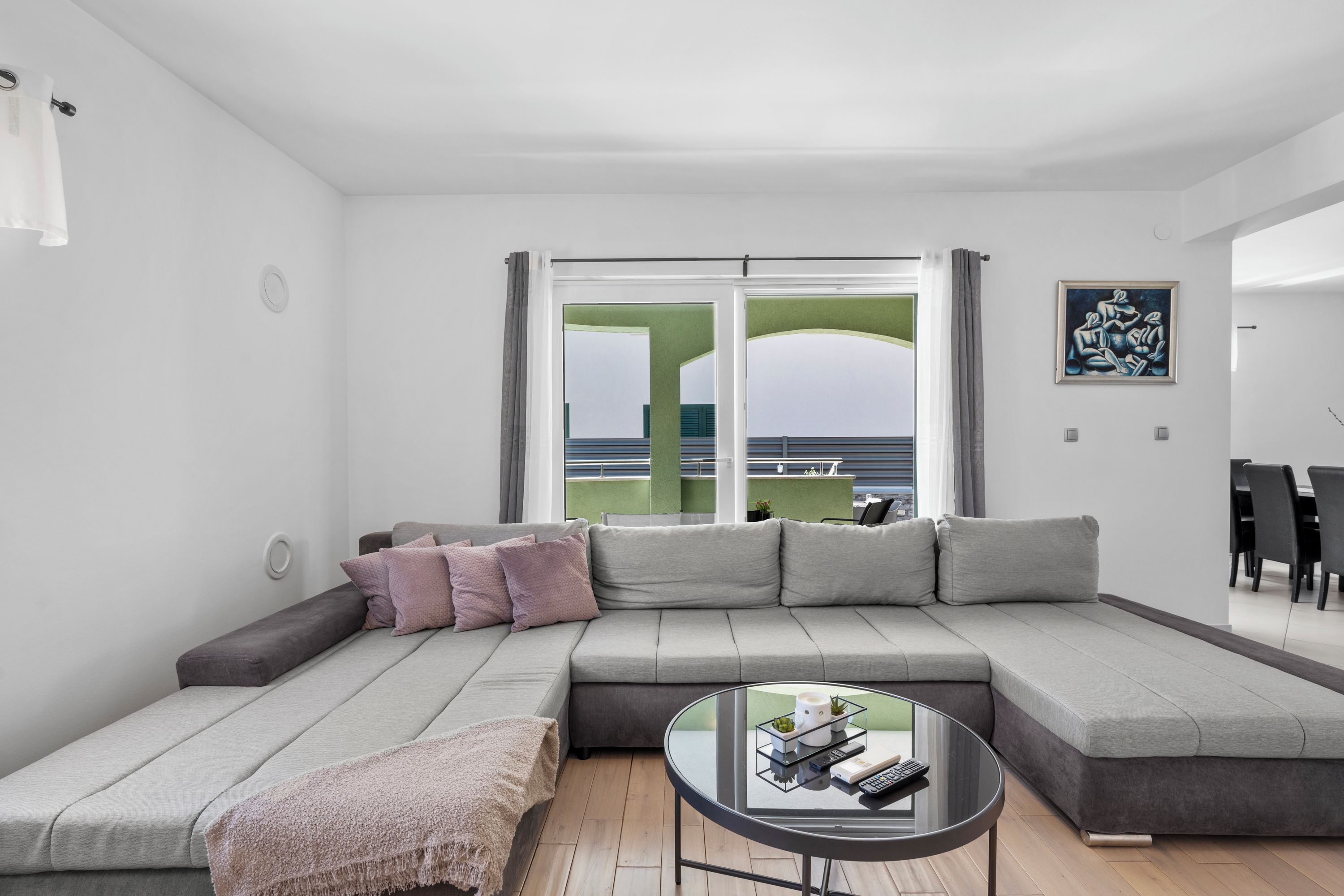 A modern living room with a sectional sofa, a glass coffee table, and a view through a large window.