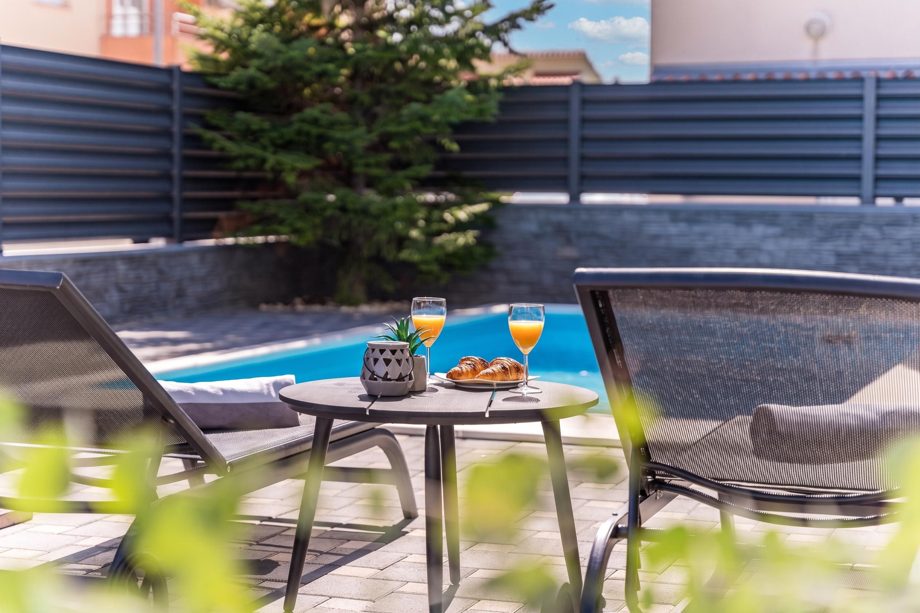 A poolside setting with lounge chairs, a table with breakfast items, and a view of the pool.