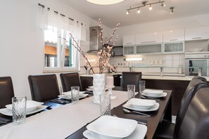 Een moderne eetruimte met een lange tafel voor zes personen, witte borden, helder glaswerk en een decoratieve vaas met takken.