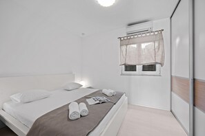 Ein Schlafzimmer mit einem Bett, einem Fenster mit Vorhang, einer Klimaanlage und einer Zeitschrift auf dem Bett.