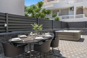 An outdoor dining area with a table set for four, surrounded by chairs, a vase with flowers, and a hot tub in the background. - S Villa With Pool, Jacuzzi & Gym (Vodice)
