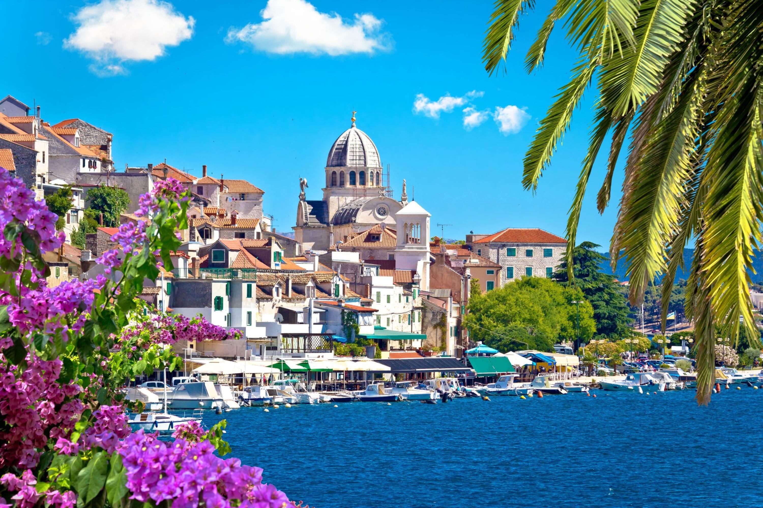 A coastal town with historic buildings, a prominent church with a dome, and a marina with boats.