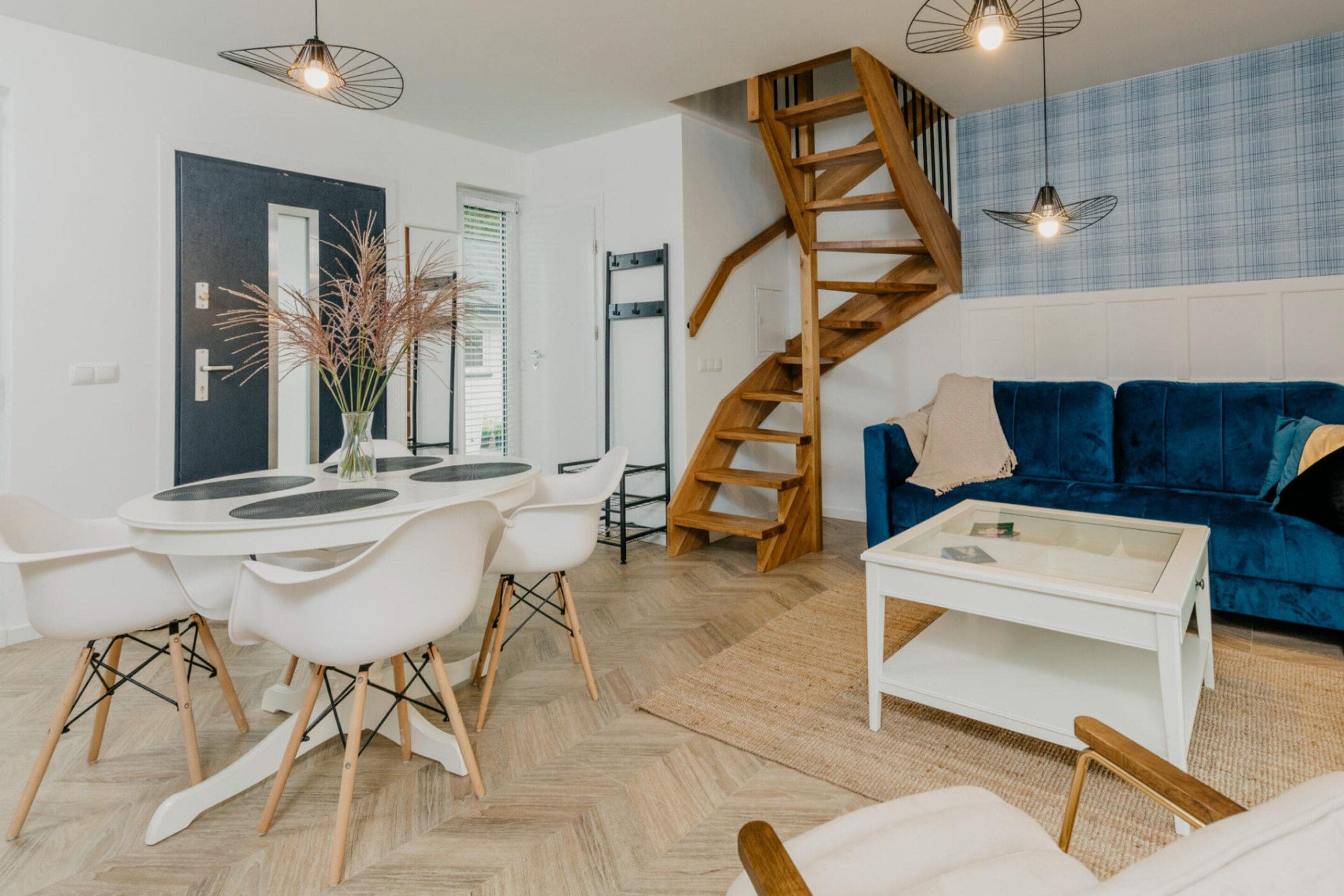 A modern living room with a blue sofa, a white coffee table, and a dining area with white chairs and a round table.