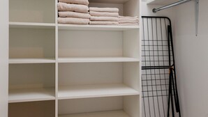 Ein weißer Kleiderschrank mit Regalen, einer Kleiderstange und gefalteten Handtüchern.