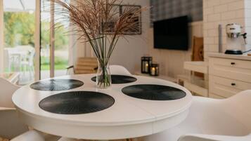 Una mesa de comedor redonda con un jarrón blanco que contiene plantas secas, rodeada de sillas blancas.