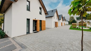 Eine Reihe moderner Häuser mit einem gepflasterten Weg, Holzelementen und blauem Himmel.