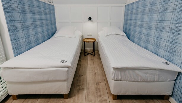 Ein Zimmer mit zwei Einzelbetten, einem kleinen runden Tisch und einer Wandleuchte.