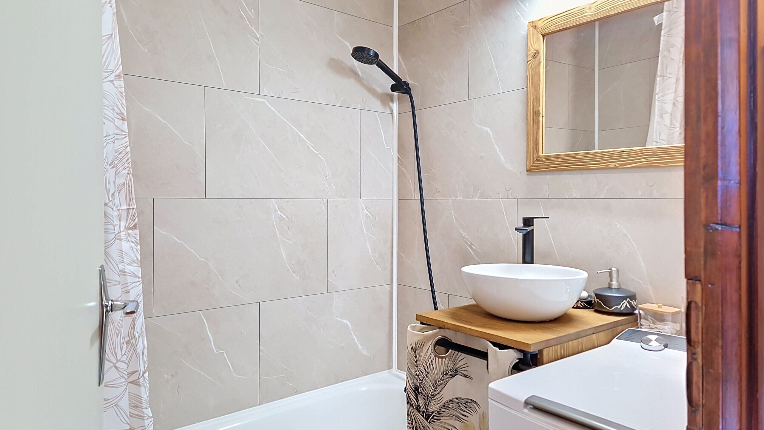 Un baño con bañera, lavamanos de cuenca grande, cabezal de ducha de mano y estante de madera con lavabo.