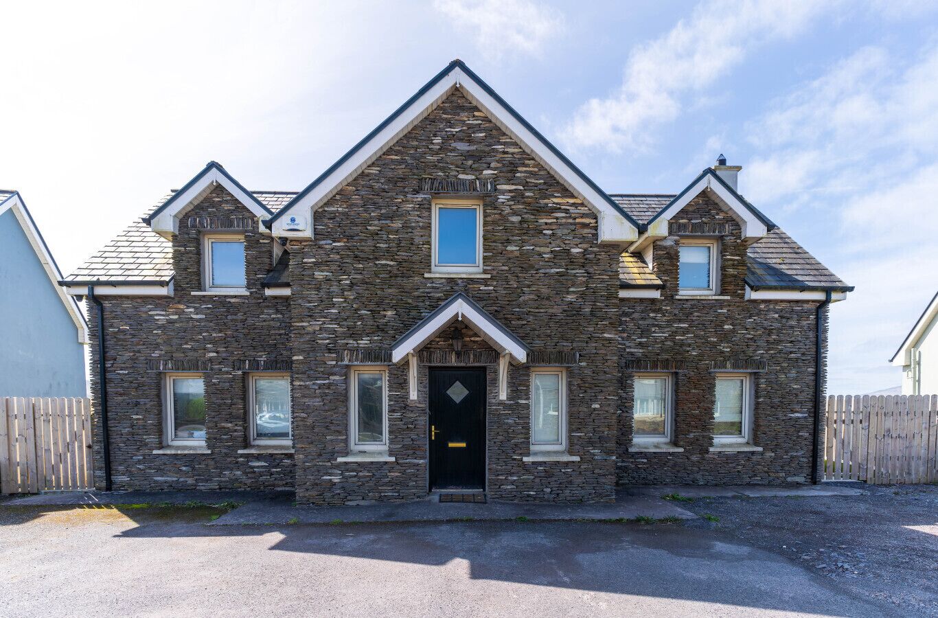 A two-story stone house with a black front door, multiple windows, and a sloped roof.