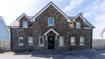 A two-story stone house with a black front door, multiple windows, and a sloped roof.