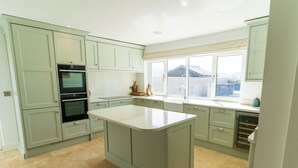 A kitchen with light green cabinets, a central island, a built-in oven, and a window with a view. - 5 The Cloisters - Waterville (Waterville)