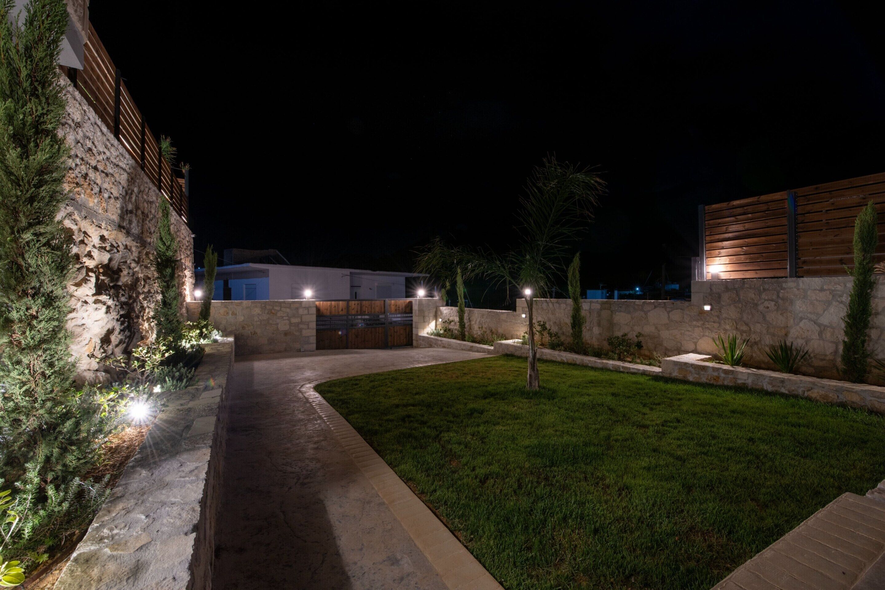 Un espace extérieur aménagé pour la nuit, avec un mur en pierre, une clôture en bois et un chemin bien éclairé.