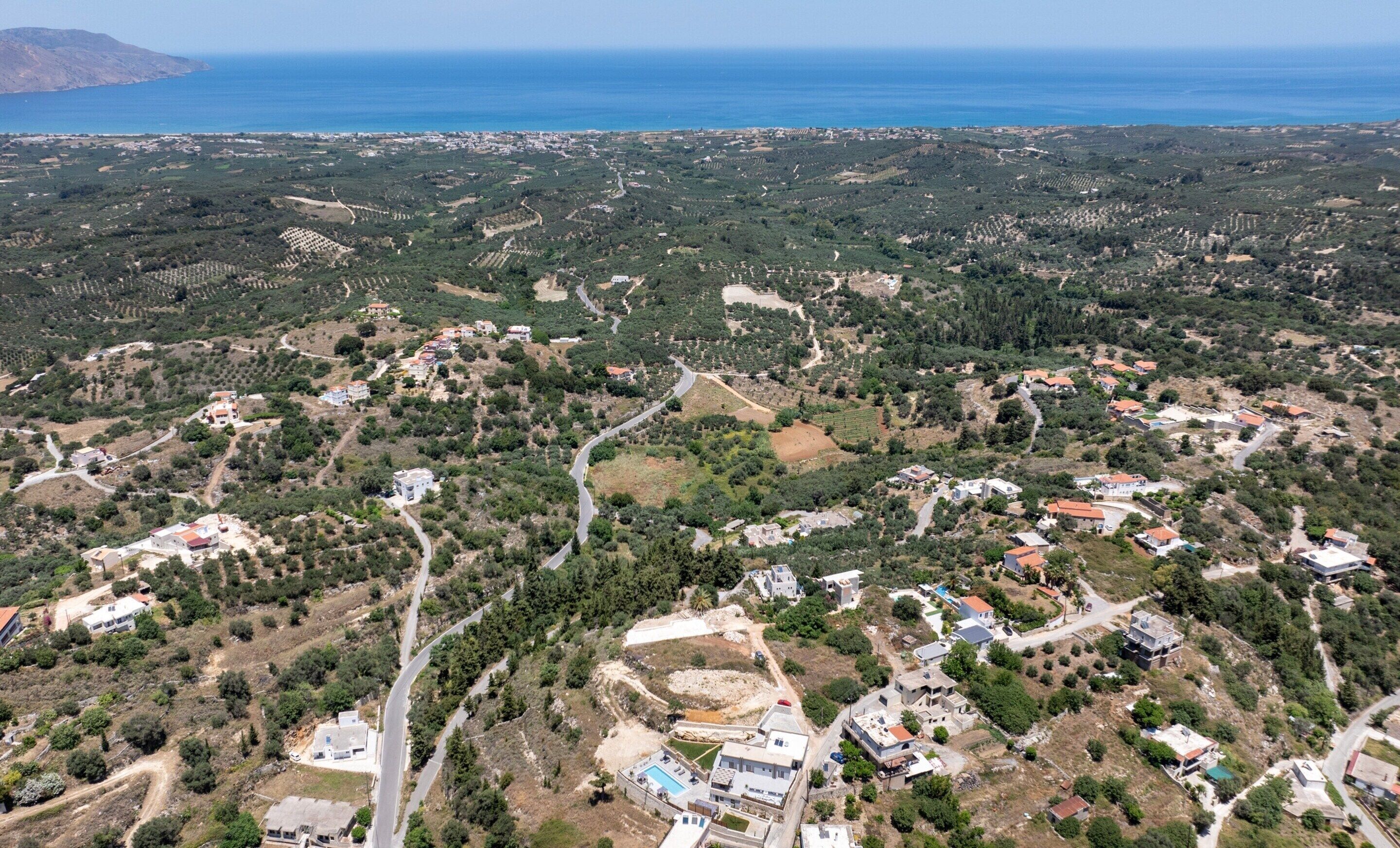 Vue aérienne d’une zone côtière parsemée de bâtiments, de routes et d’oliveraies.