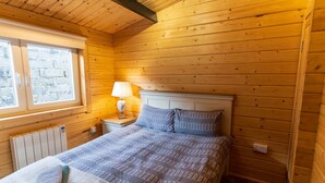 Ein Schlafzimmer einer Holzhütte mit Bett, Nachttisch mit Lampe, Fenster und Heizkörper.