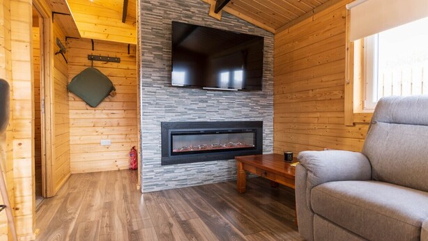 Ein gemütliches Blockhauskaminzimmer mit Kamin, einer Couch und einem an einer Steinwand befestigten Fernseher.