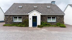 Een stenen huis met een blauwe deur, een grindpad en een kleine tuin.