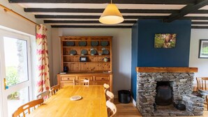 Een eethoek met een houten tafel en stoelen, een stenen openhaard en een houten kast met servies.