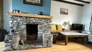 A stone fireplace with a wooden mantel, a television, and a sofa in a living room with wooden flooring. - Skellig Cottage - Portmagee (Portmagee)