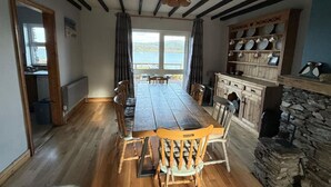 A dining room with a wooden table and chairs, a stone fireplace, and a view of the outdoors. - Skellig Cottage - Portmagee (Portmagee)