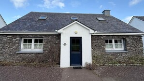 A stone house with a dark roof, a central entrance, and two windows on either side. - Skellig Cottage - Portmagee (Portmagee)